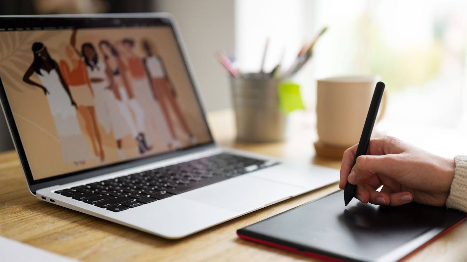 Digital artist working on tablet and laptop to create commissioned artwork for freelance illustration clients.