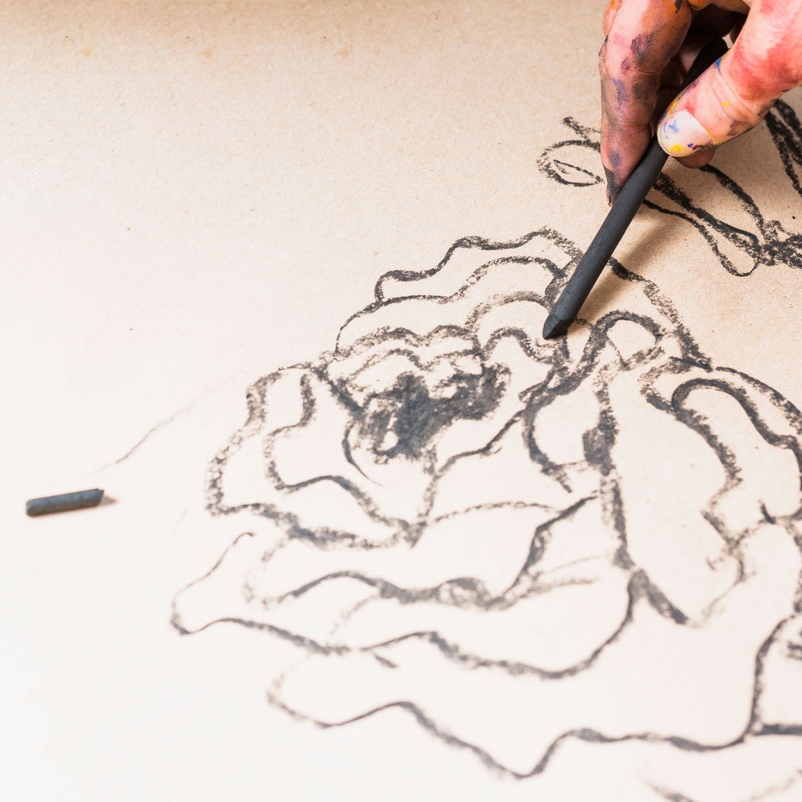 Hand drawing an abstract design with charcoal, showcasing experimenting with art styles and expressive mark-making.