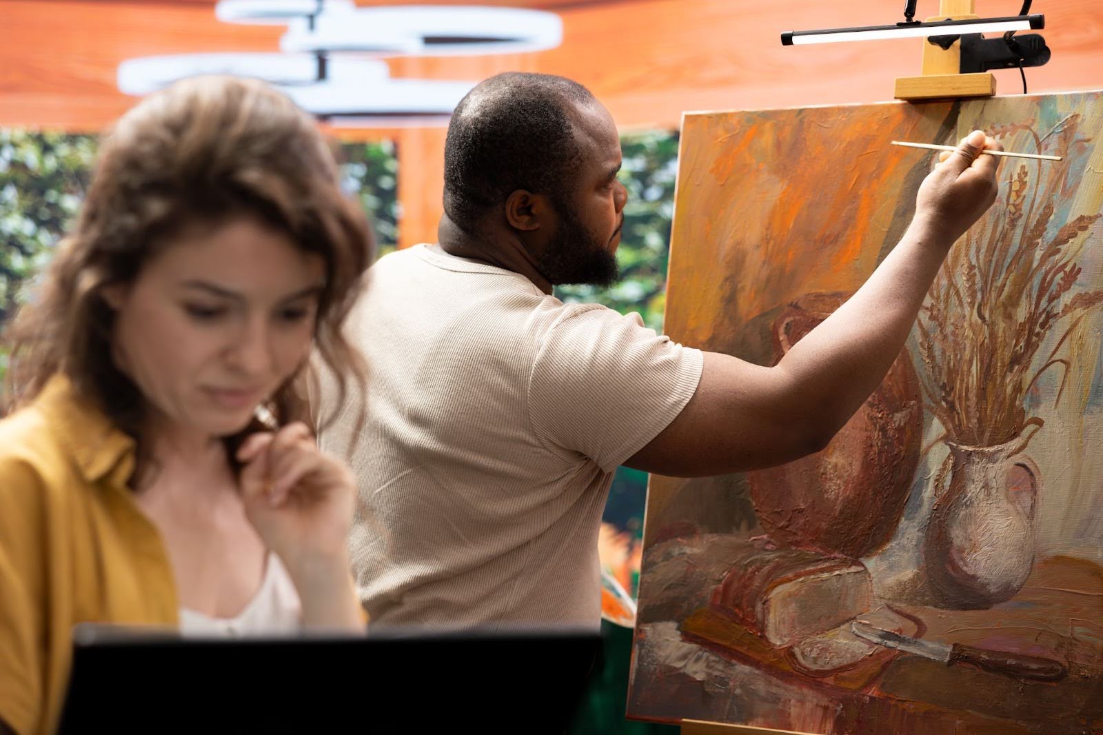 Artist researching visual references online while another paints on canvas, highlighting cross-disciplinary collaboration and creative experimentation.